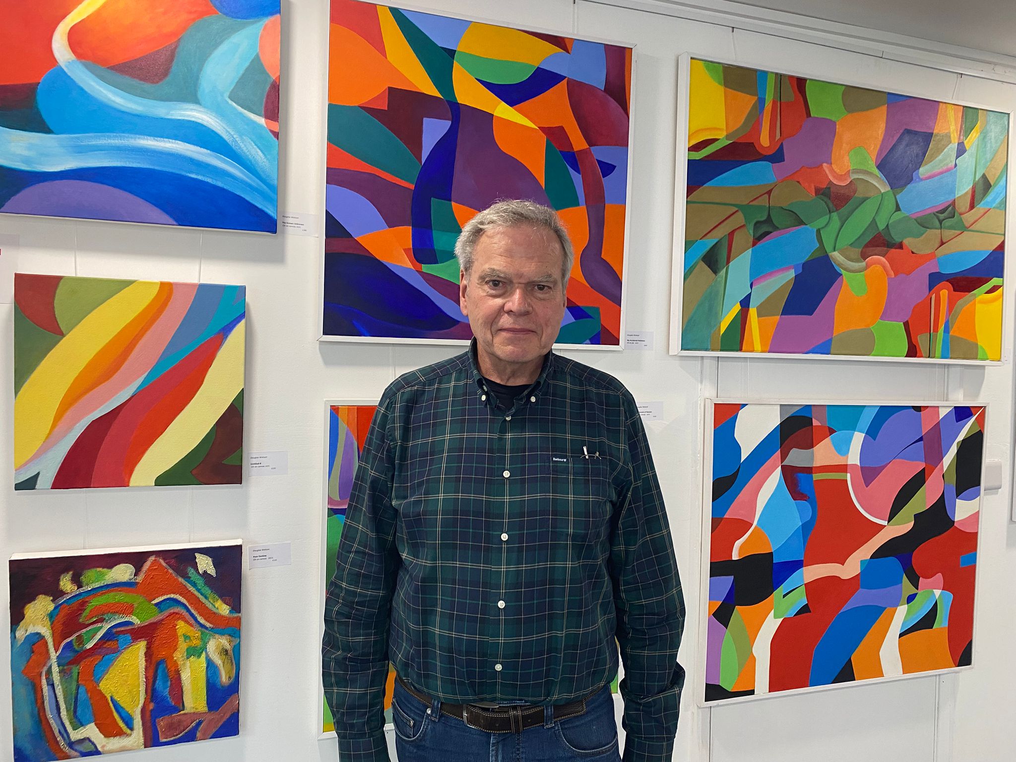 Douglas Watson standing in front of a display of his abstract art